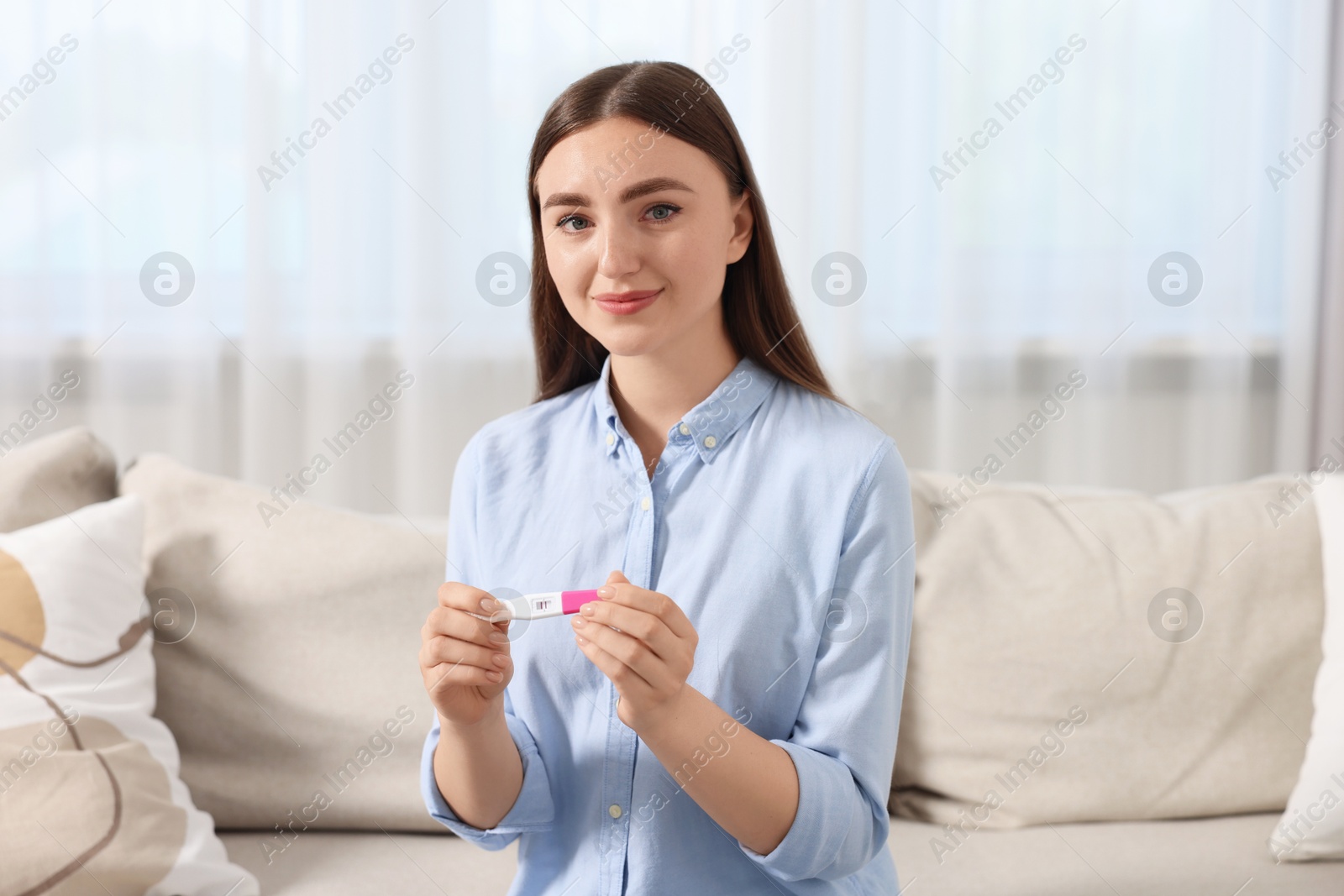 Photo of Woman holding pregnancy test on sofa indoors