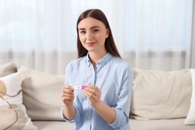 Photo of Woman holding pregnancy test on sofa indoors
