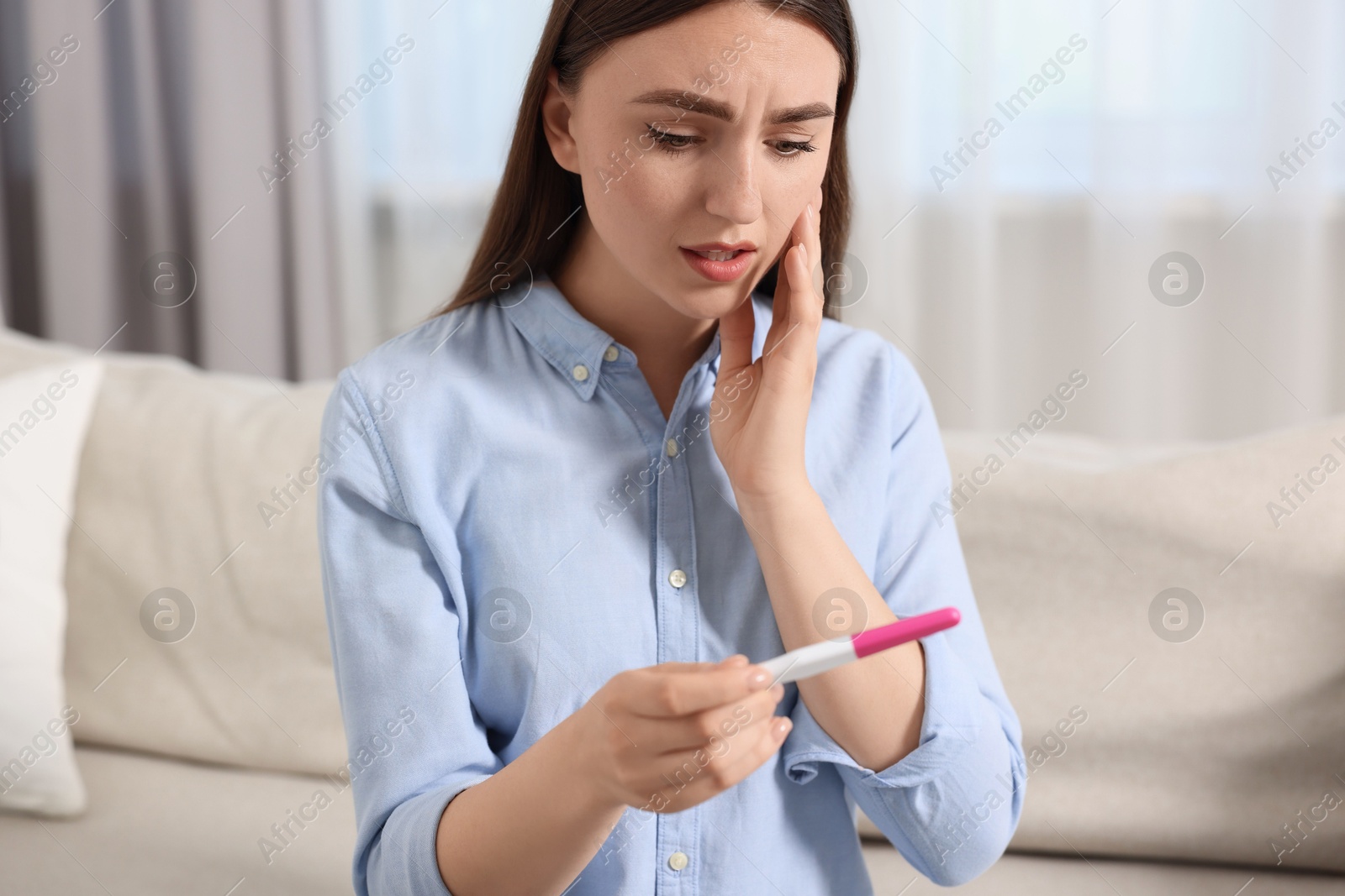 Photo of Sad woman holding pregnancy test on sofa indoors