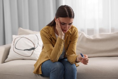 Sad woman holding pregnancy test on sofa indoors