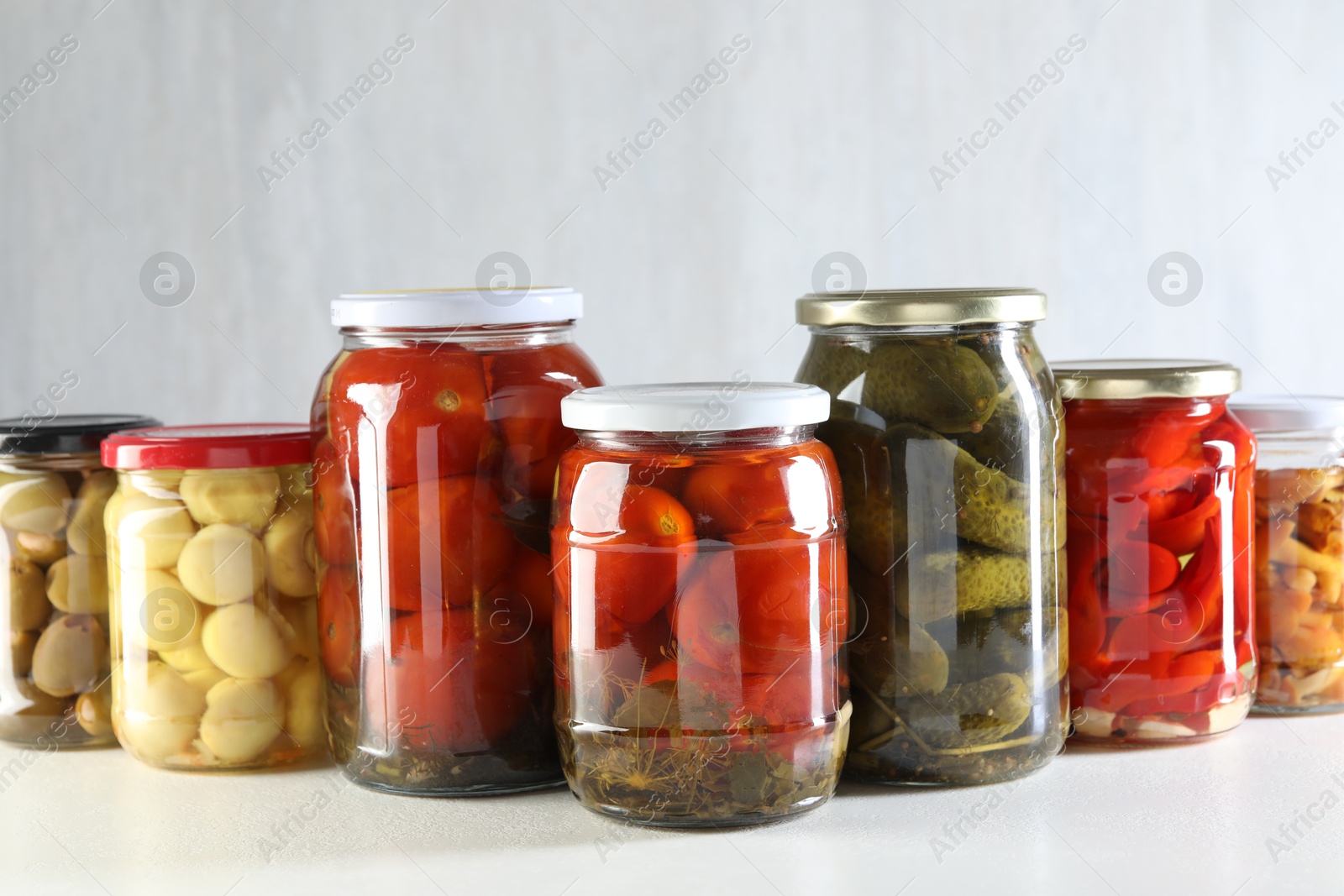 Photo of Tasty pickled vegetables and mushrooms in jars on white background