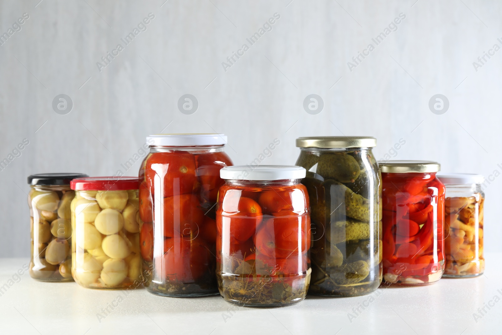 Photo of Tasty pickled vegetables and mushrooms in jars on white background