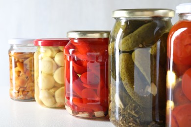 Photo of Tasty pickled vegetables and mushrooms in jars on white background, closeup