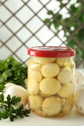 Photo of Tasty pickled mushrooms in jar and parsley on white table indoors