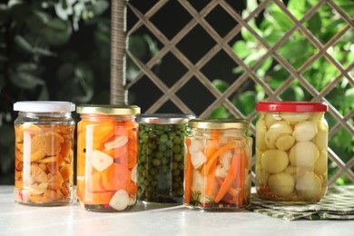 Photo of Tasty pickled vegetables and mushrooms in jars on white background