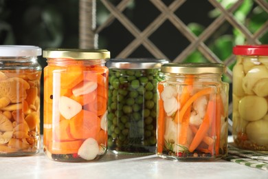 Photo of Tasty pickled vegetables and mushrooms in jars on white table indoors