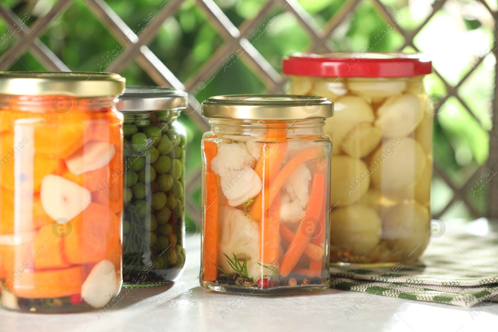 Photo of Tasty pickled vegetables and mushrooms in jars on white table indoors, closeup