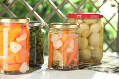 Photo of Tasty pickled vegetables and mushrooms in jars on white table indoors, closeup