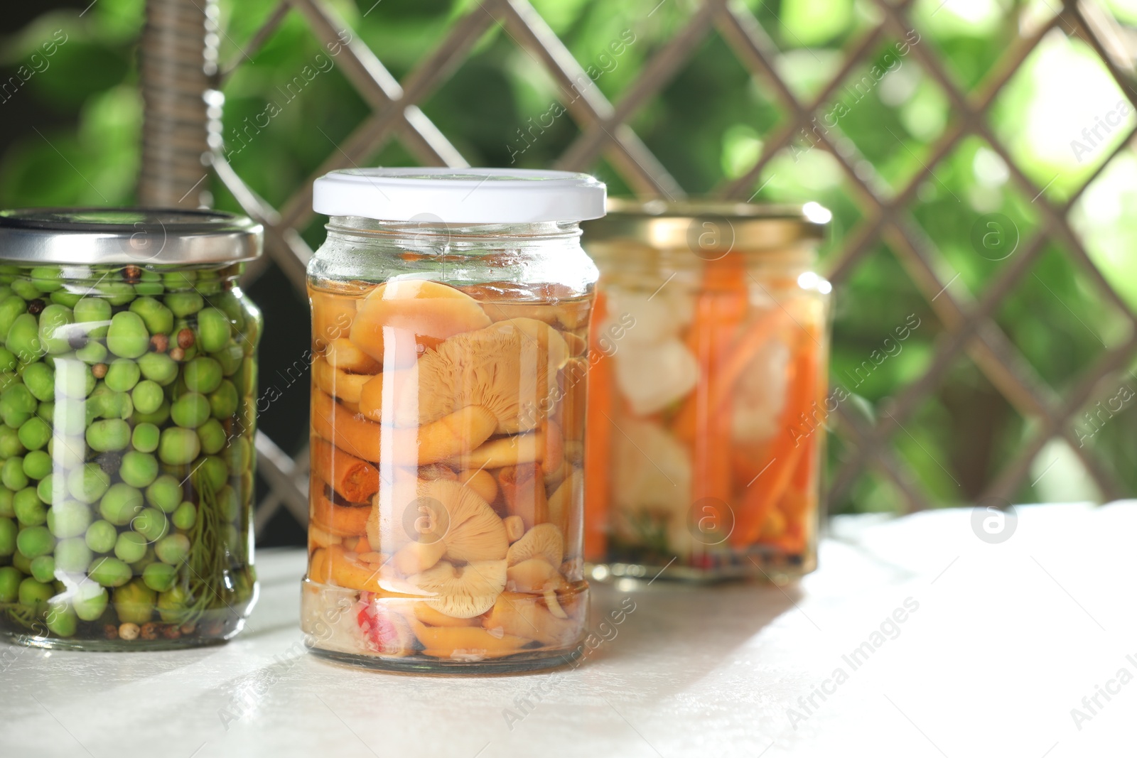 Photo of Tasty pickled vegetables and mushrooms in jars on white table indoors