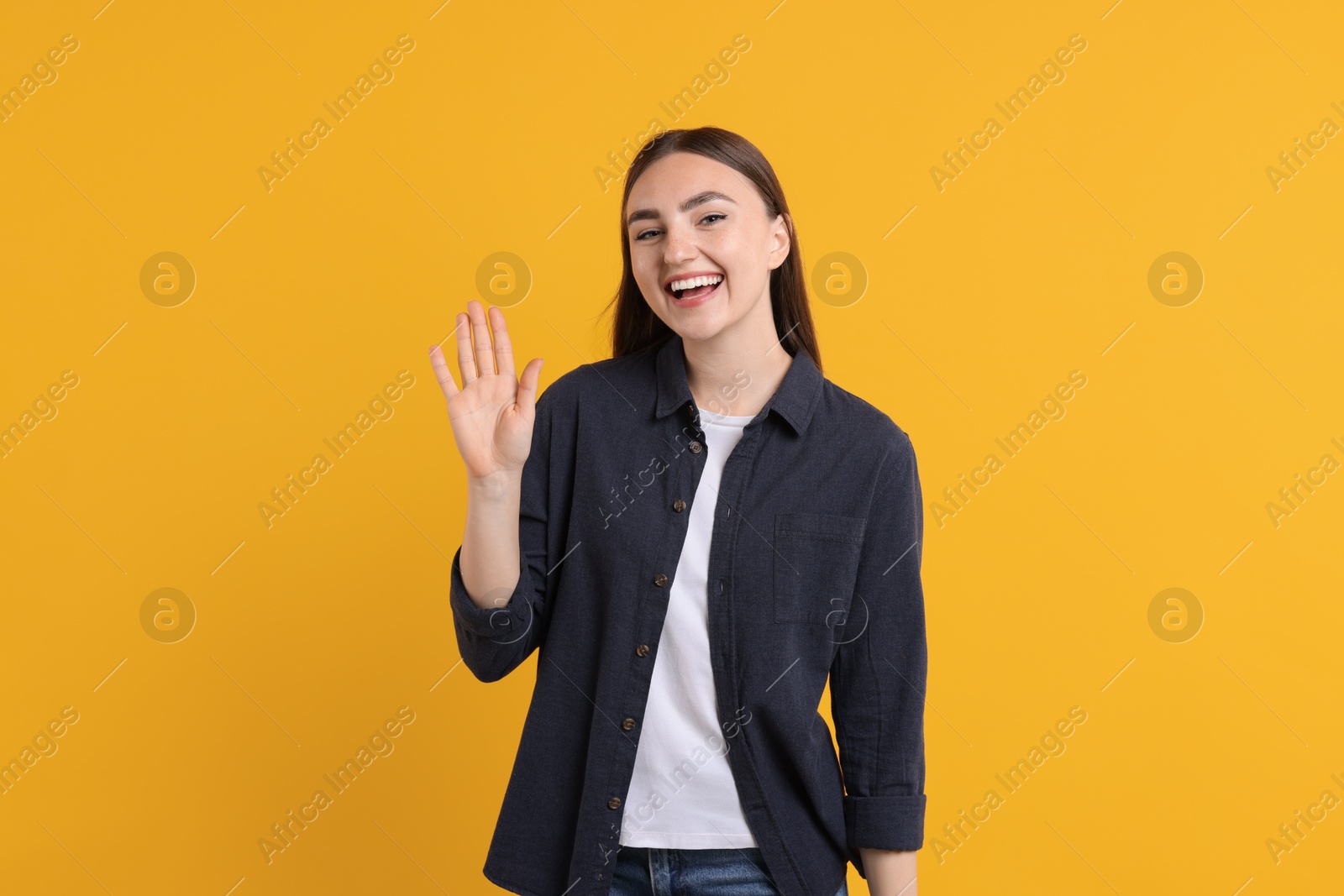 Photo of Happy young woman waving on orange background