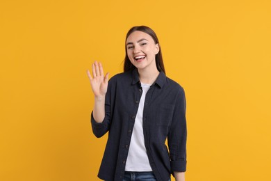 Photo of Happy young woman waving on orange background