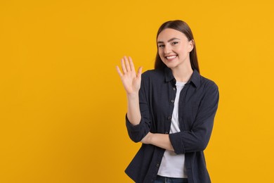 Photo of Happy young woman waving on orange background, space for text