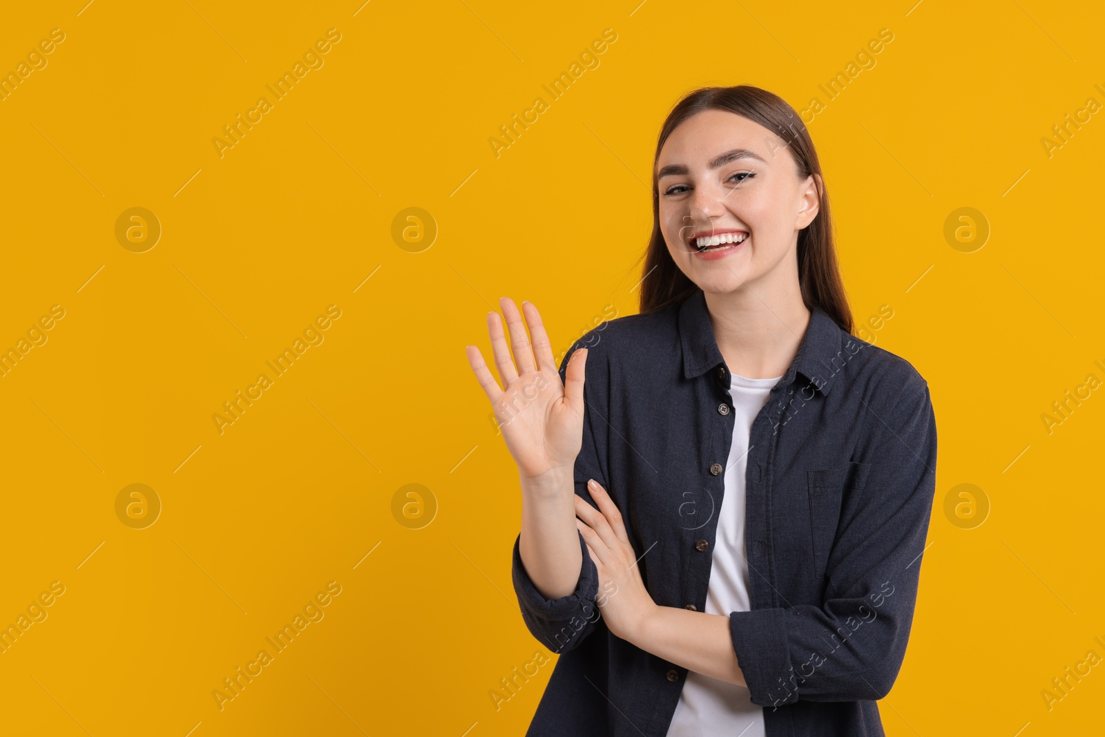 Photo of Happy young woman waving on orange background, space for text