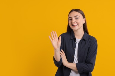 Photo of Happy young woman waving on orange background, space for text