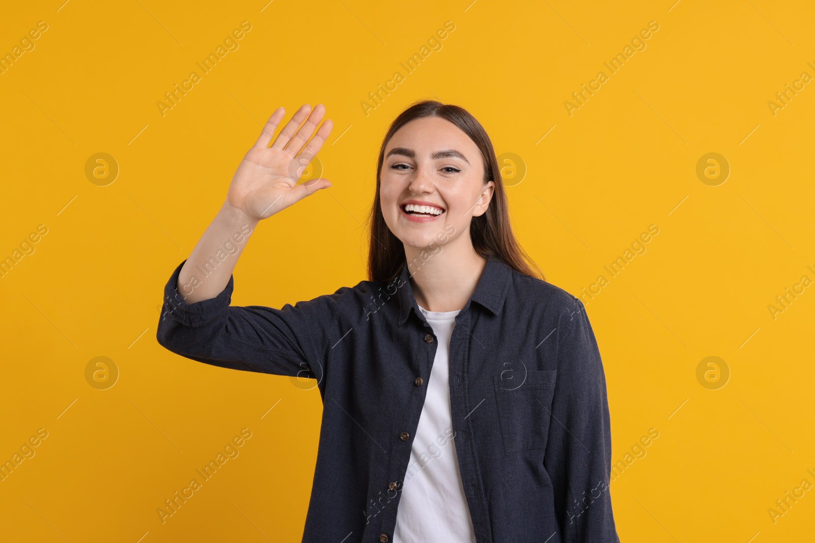 Photo of Happy young woman waving on orange background