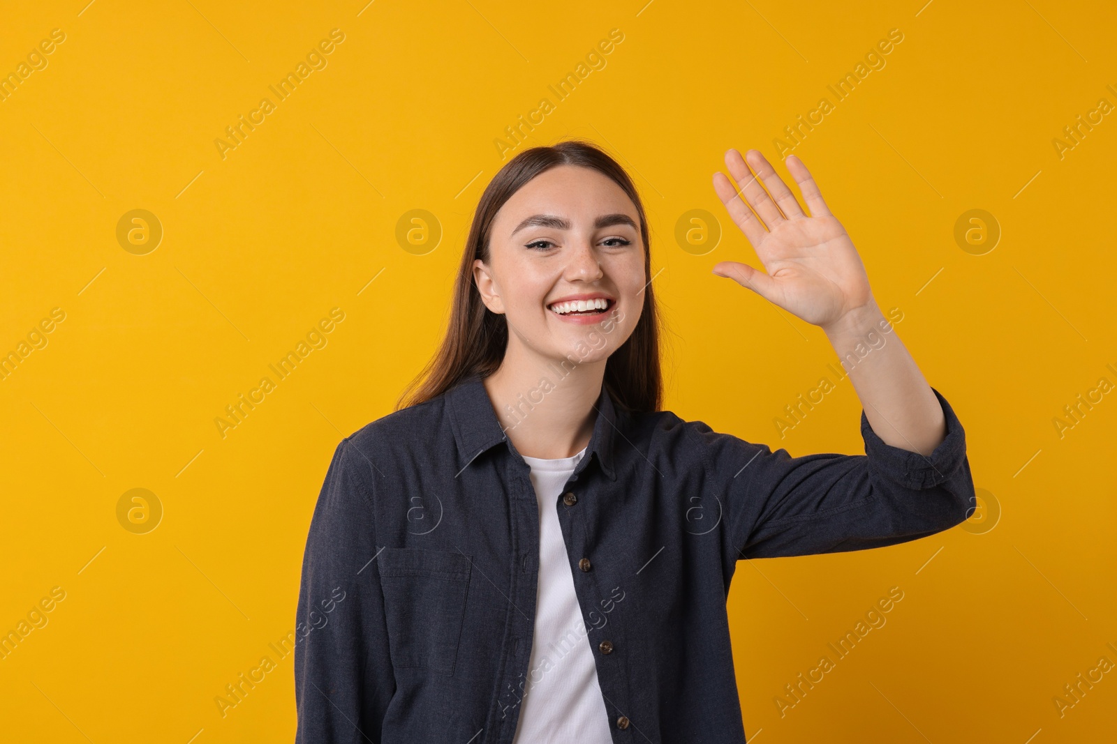 Photo of Happy young woman waving on orange background