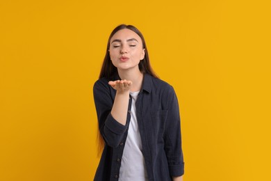 Beautiful woman blowing kiss on orange background