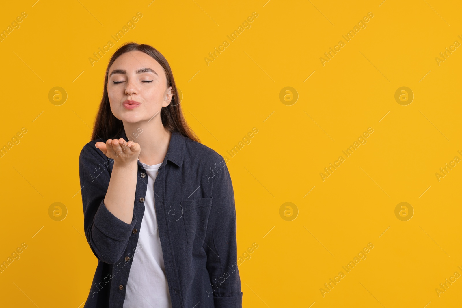 Photo of Beautiful woman blowing kiss on orange background, space for text