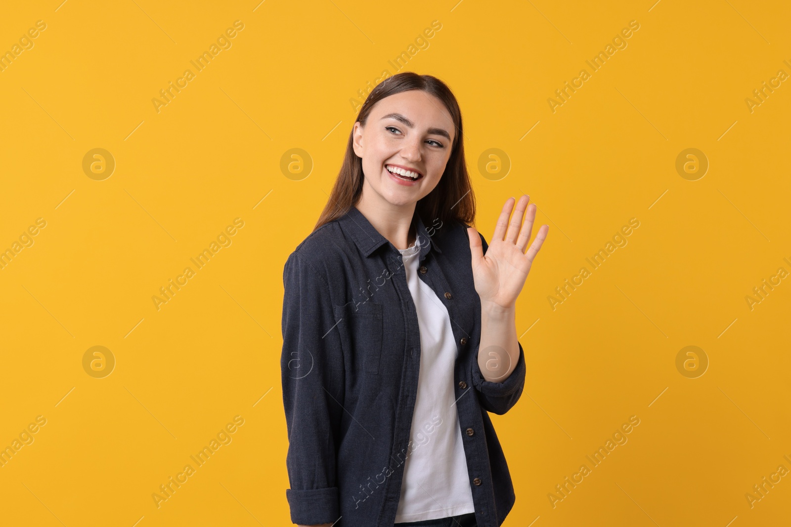 Photo of Happy young woman waving on orange background