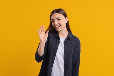 Happy young woman waving on orange background