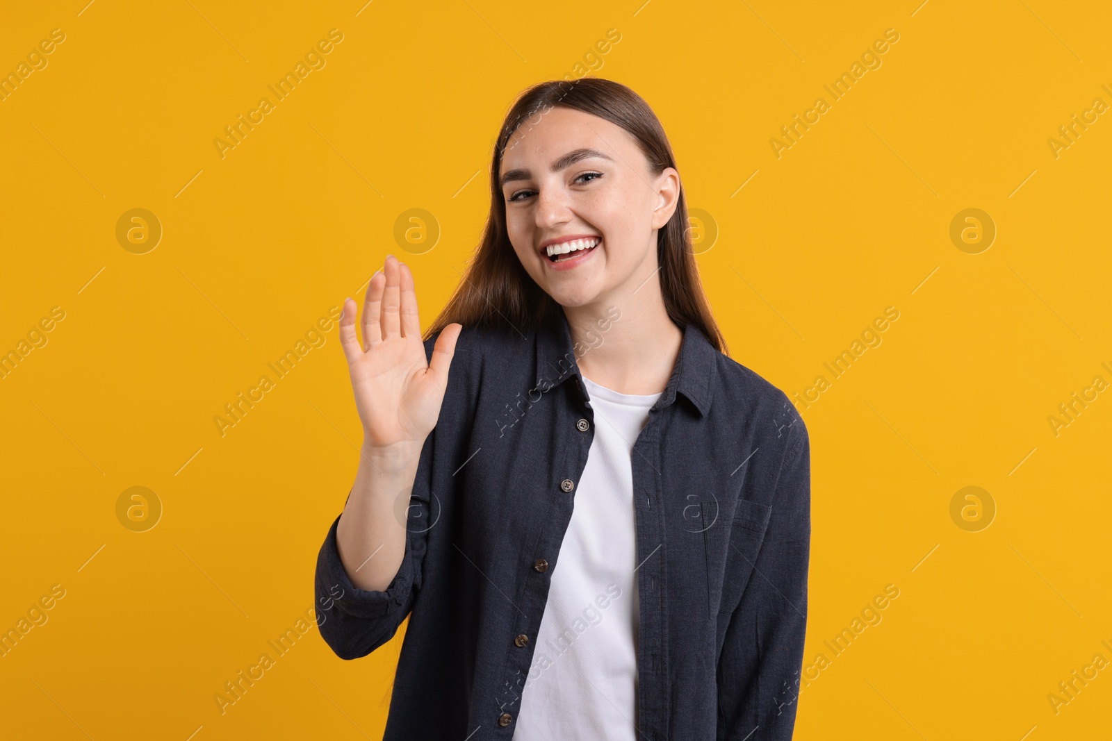 Photo of Happy young woman waving on orange background