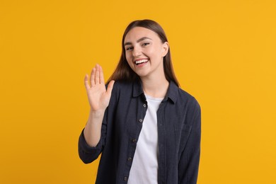 Happy young woman waving on orange background