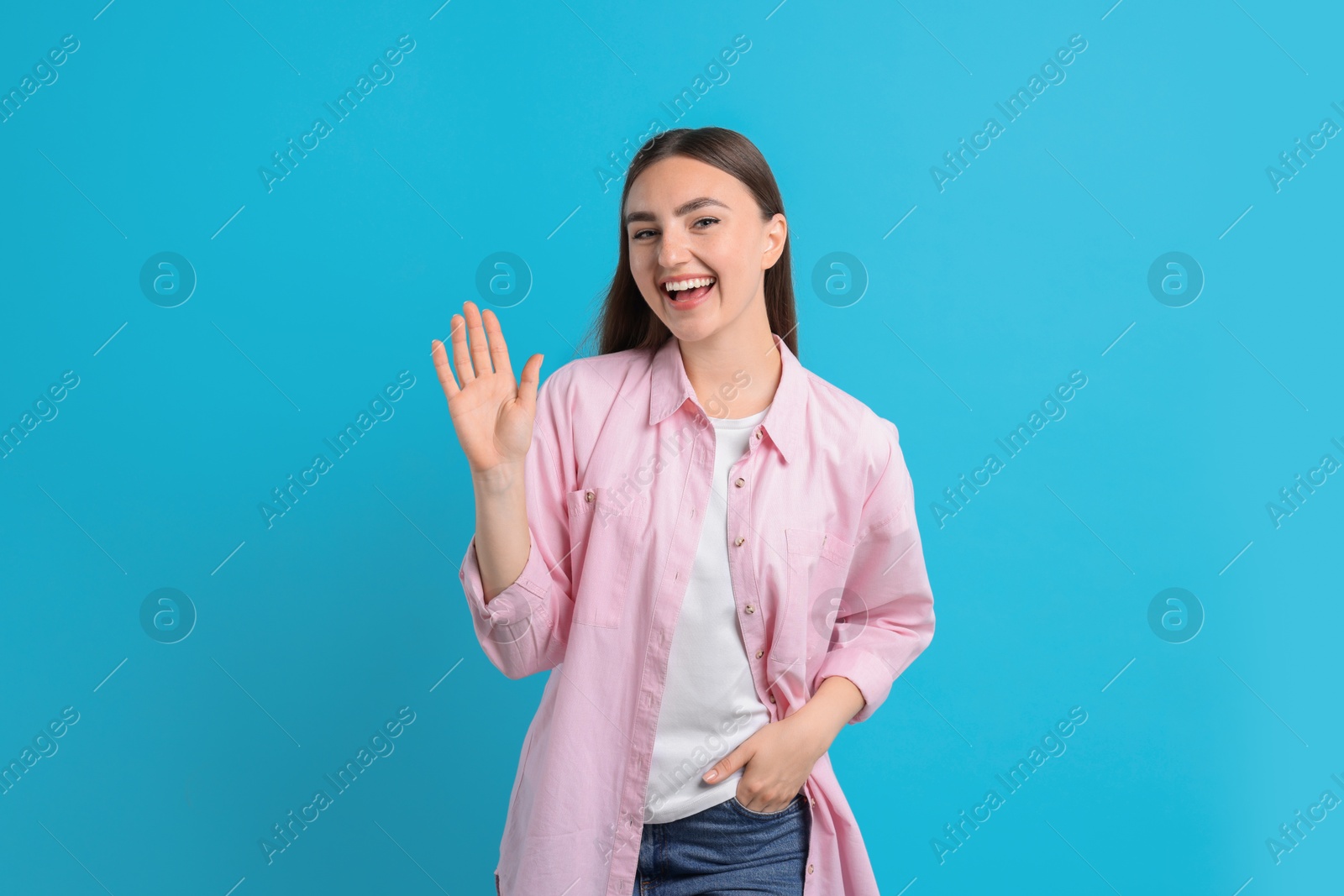 Photo of Happy woman waving on light blue background