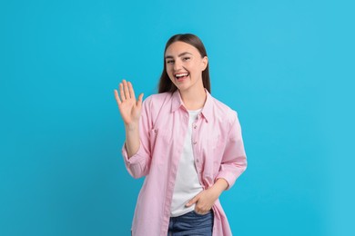 Happy woman waving on light blue background