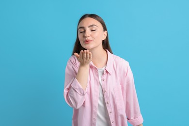 Beautiful woman blowing kiss on light blue background