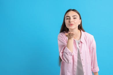 Beautiful woman blowing kiss on light blue background, space for text