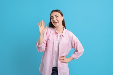 Photo of Happy woman waving on light blue background