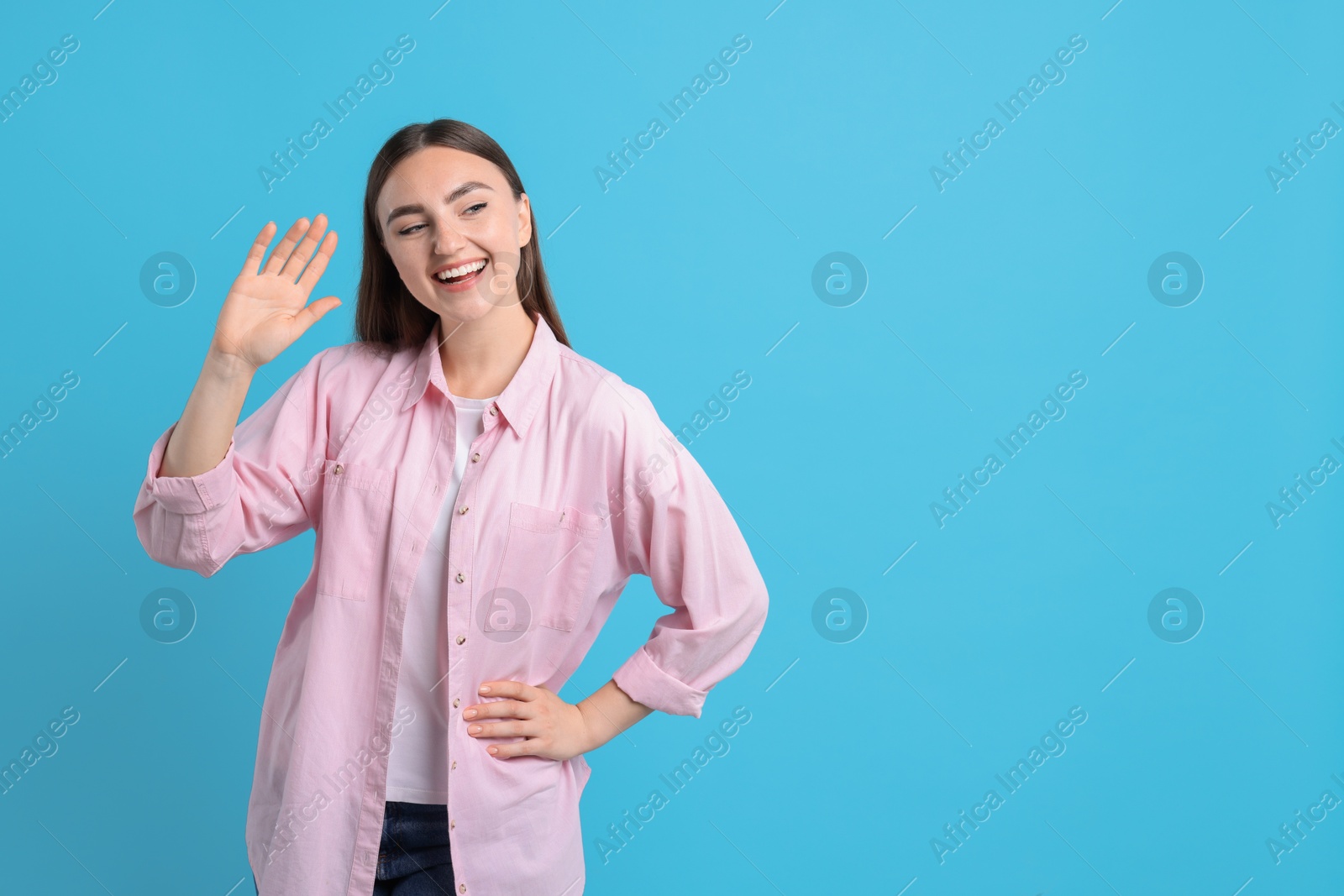 Photo of Happy woman waving on light blue background, space for text