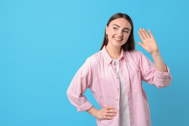 Happy woman waving on light blue background, space for text