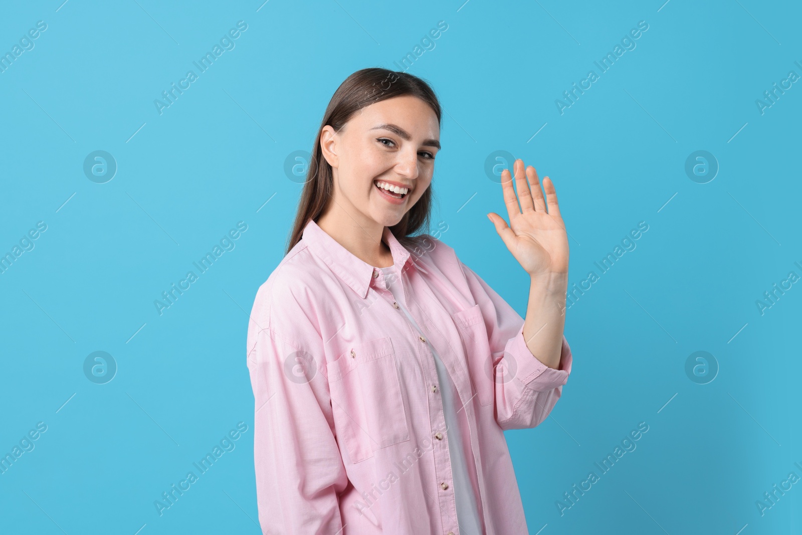 Photo of Happy woman waving on light blue background