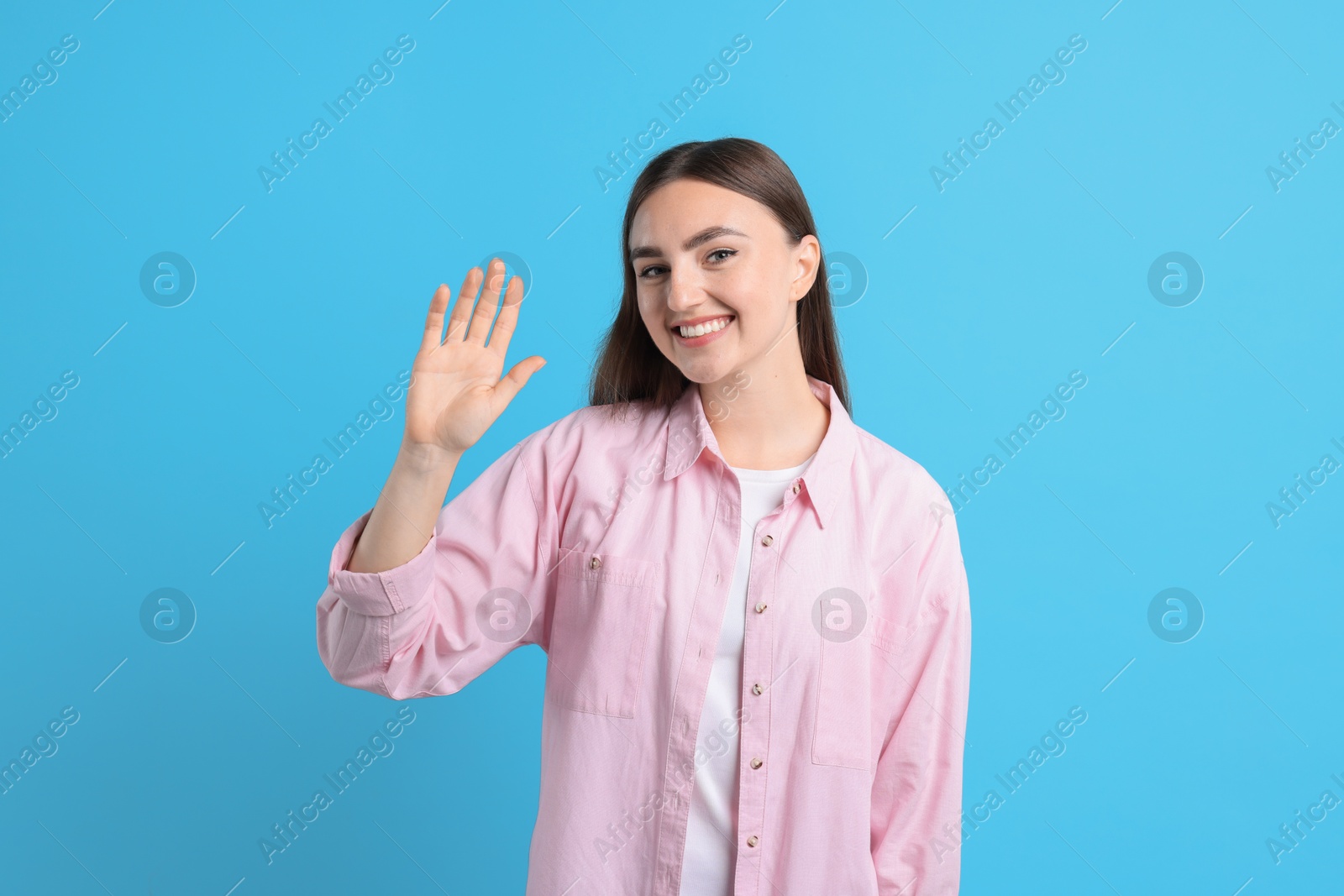 Photo of Happy woman waving on light blue background