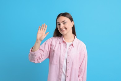 Photo of Happy woman waving on light blue background