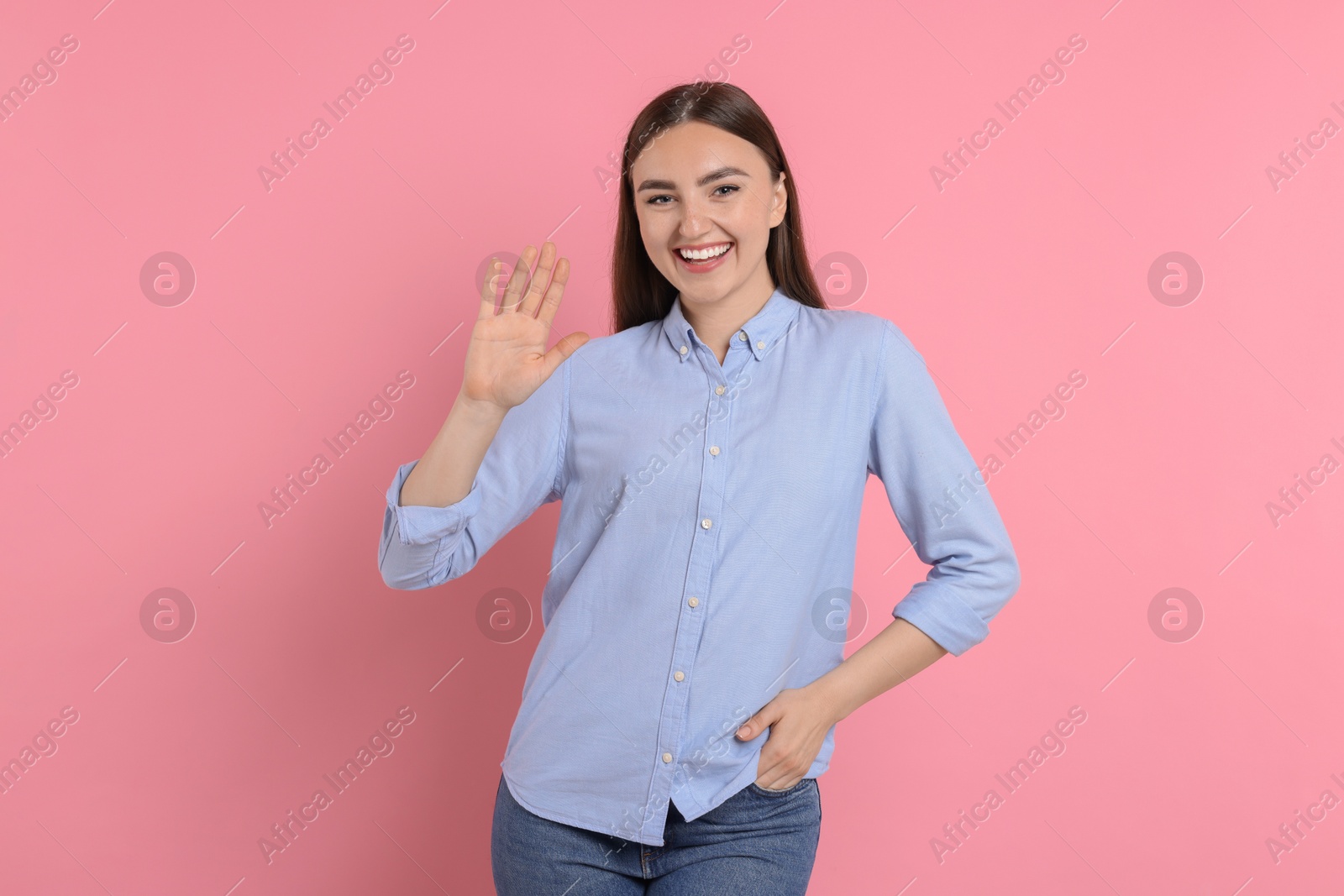 Photo of Happy young woman waving on pink background