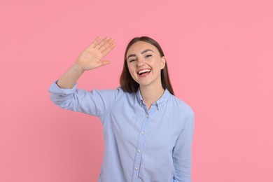 Photo of Happy young woman waving on pink background