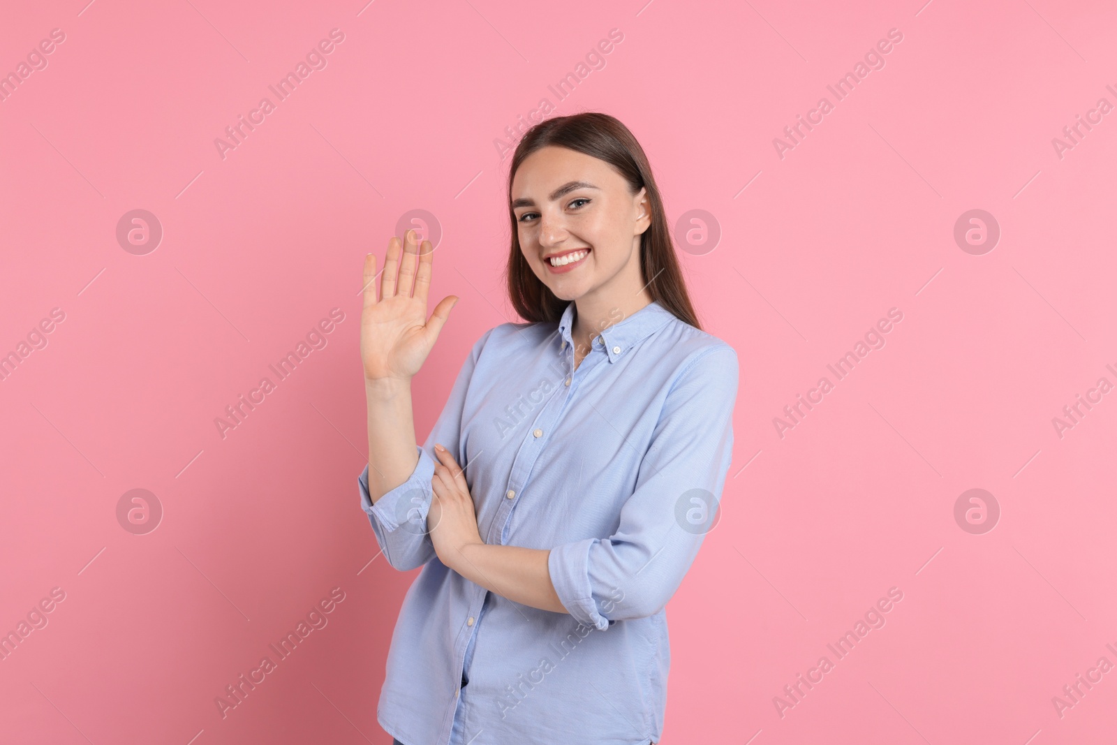 Photo of Happy young woman waving on pink background