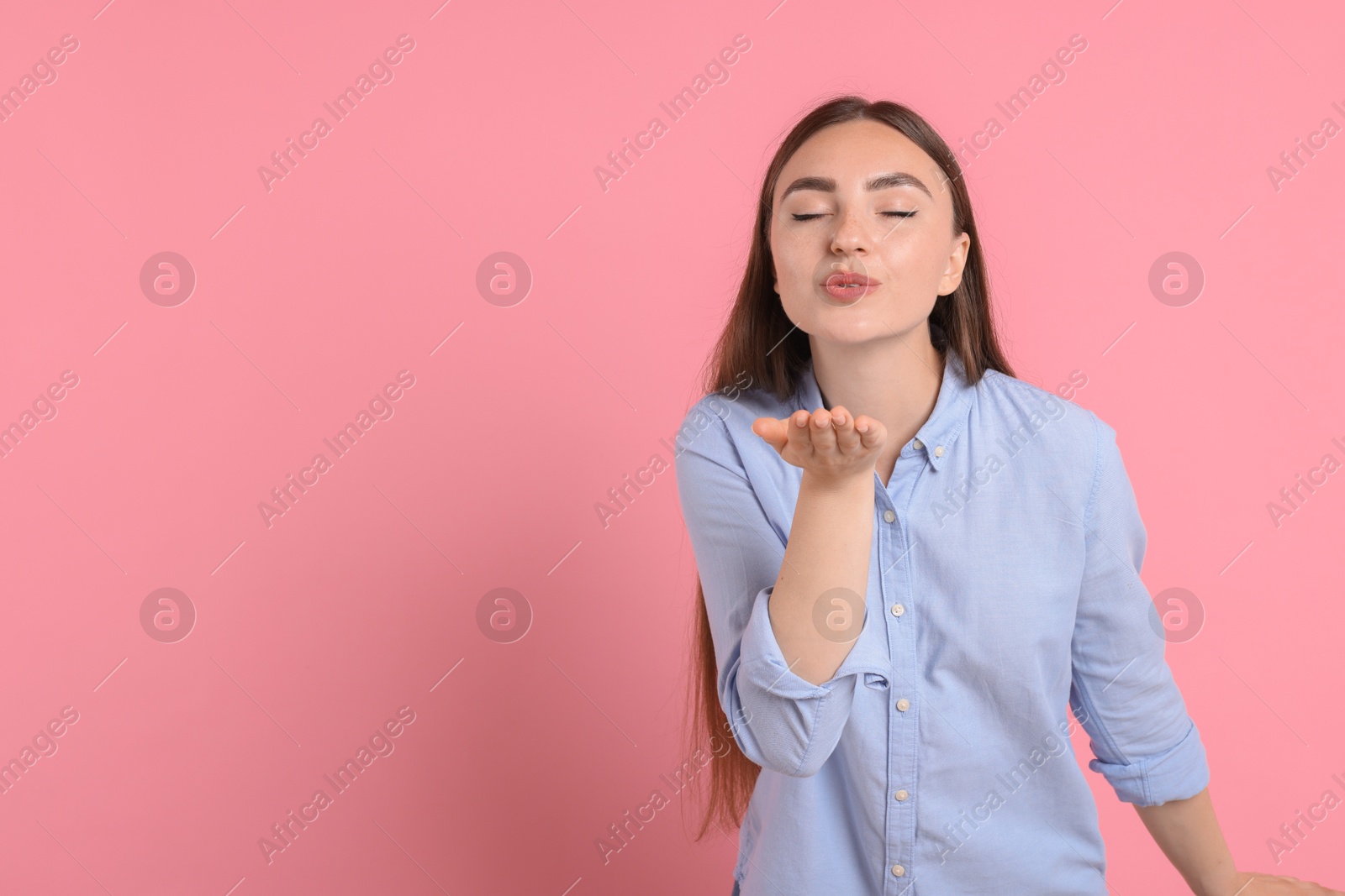 Photo of Beautiful woman blowing kiss on pink background, space for text