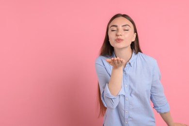 Photo of Beautiful woman blowing kiss on pink background, space for text