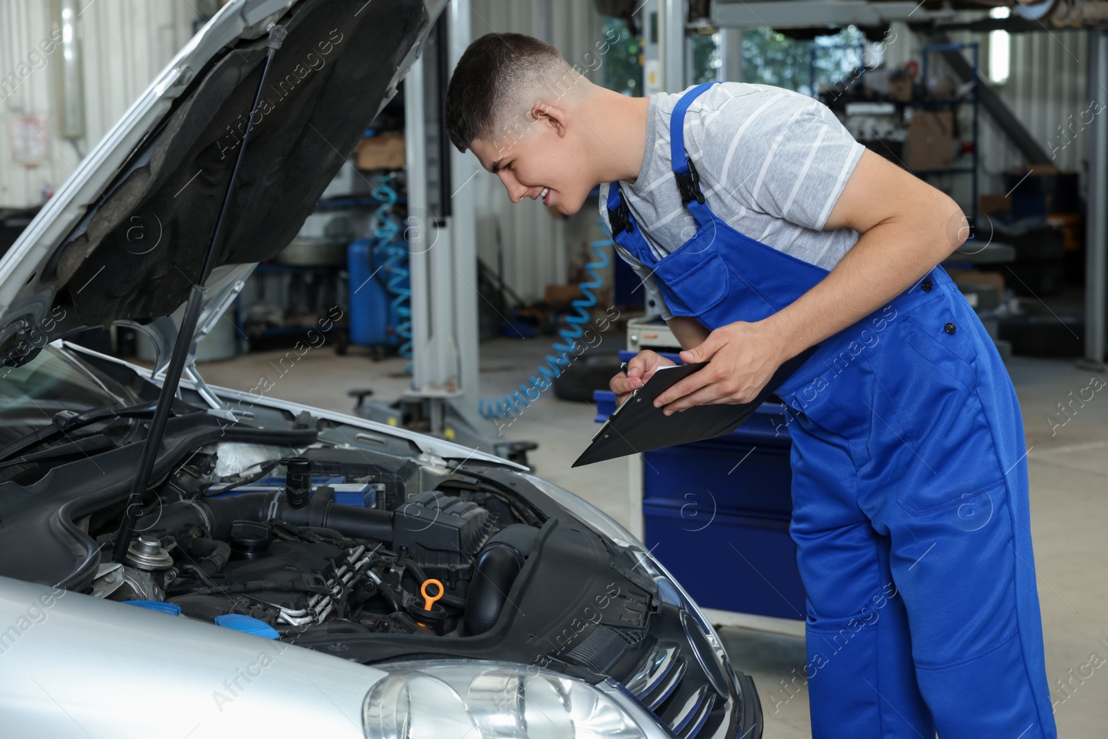 Photo of Young auto mechanic taking notes while doing car diagnostic at automobile repair shop