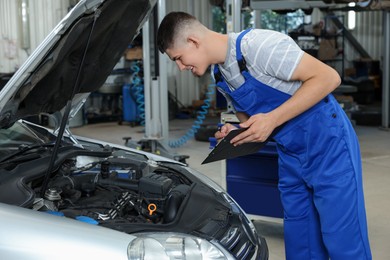 Young auto mechanic taking notes while doing car diagnostic at automobile repair shop