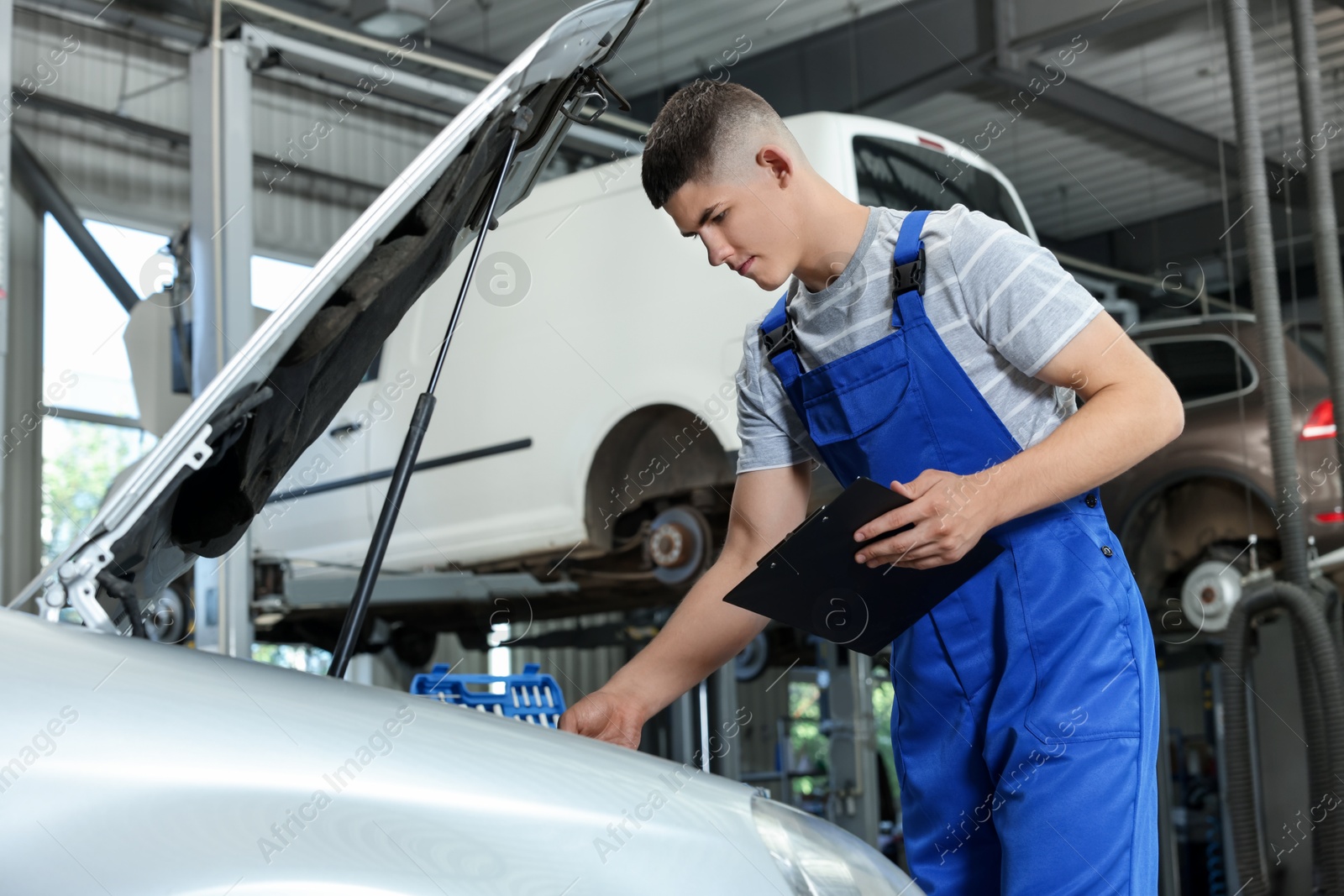 Photo of Young auto mechanic taking notes while doing car diagnostic at automobile repair shop