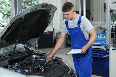 Photo of Young auto mechanic taking notes while doing car diagnostic at automobile repair shop