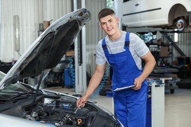 Photo of Young auto mechanic taking notes while doing car diagnostic at automobile repair shop