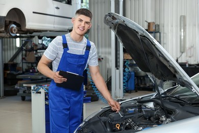 Young auto mechanic taking notes while doing car diagnostic at automobile repair shop