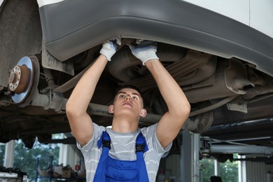 Young auto mechanic fixing lifted car at automobile repair shop