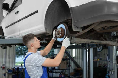 Young auto mechanic fixing lifted car at automobile repair shop