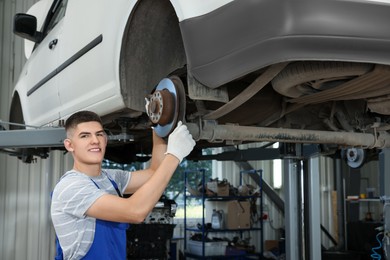 Young auto mechanic fixing lifted car at automobile repair shop